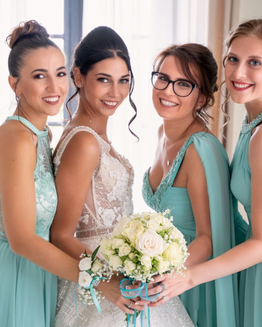 La sposa con tre damigelle in abiti verde acqua mentre sorridono insieme al bouquet