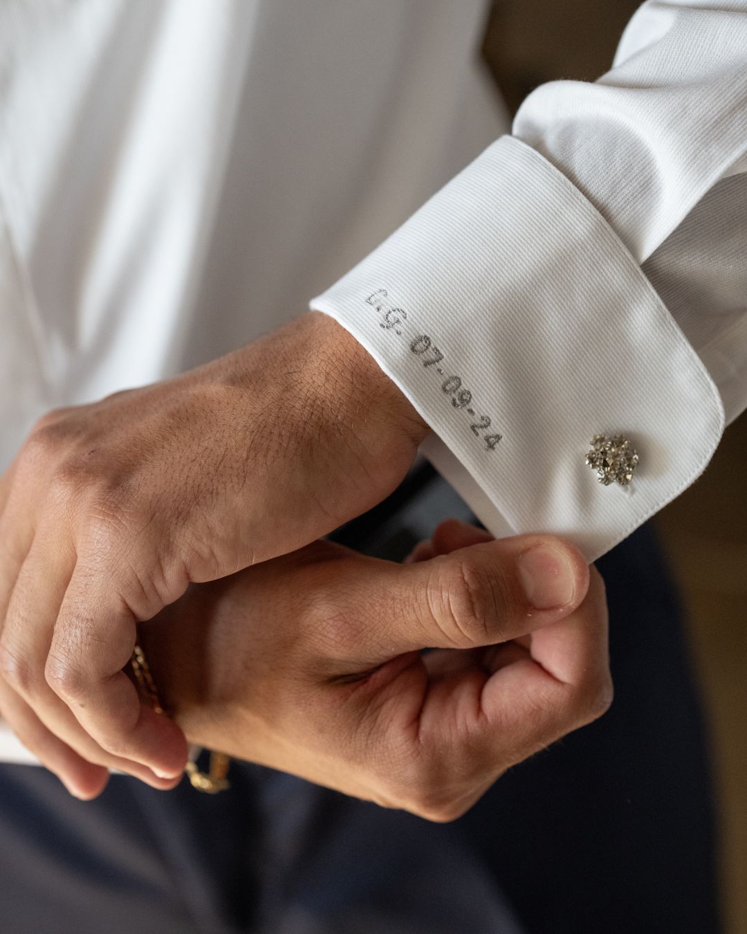 Mano dello sposo che sistema i gemelli con camicia personalizzata durante i preparativi del matrimonio