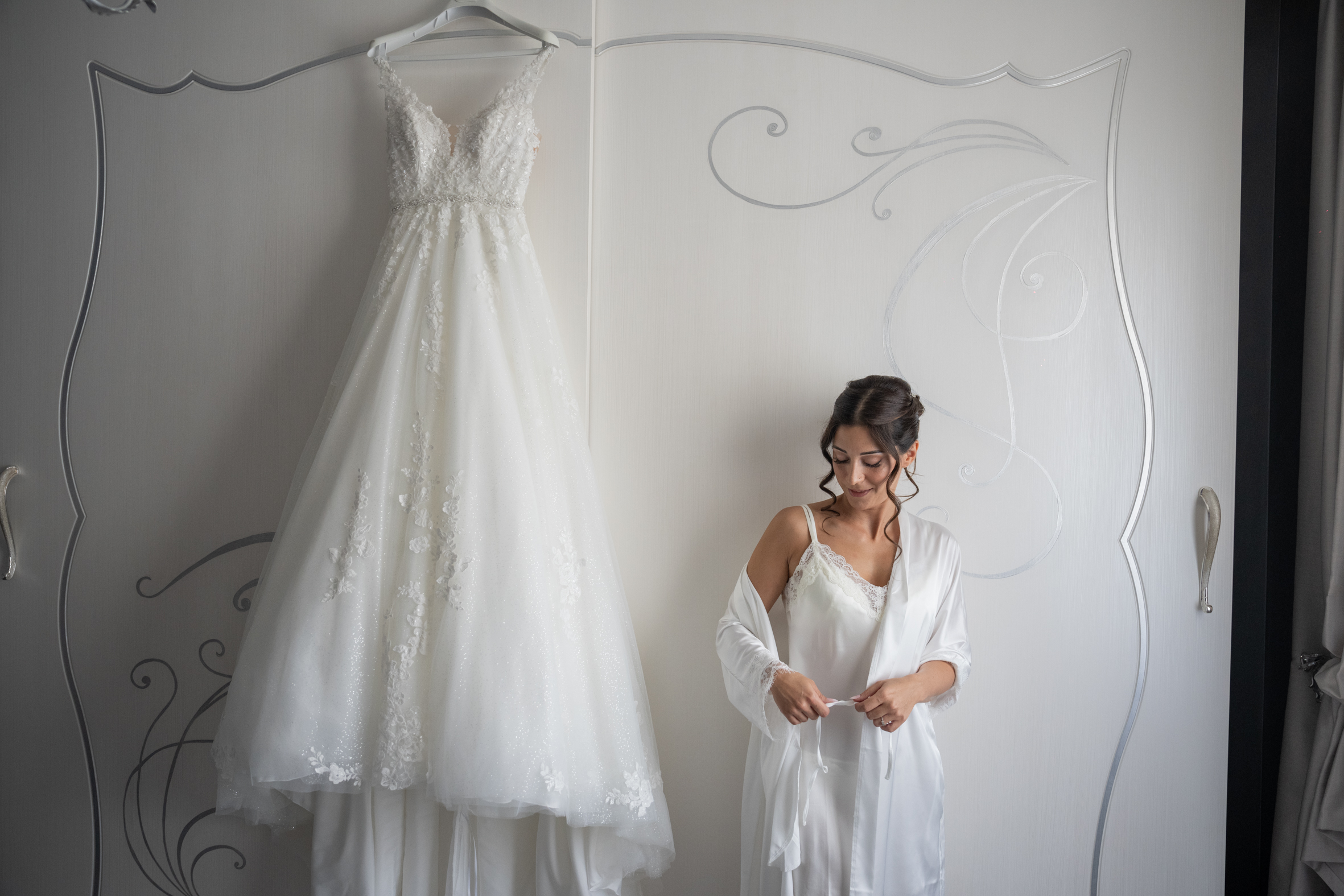 sposa in vestaglia davanti all’abito da sposa appeso