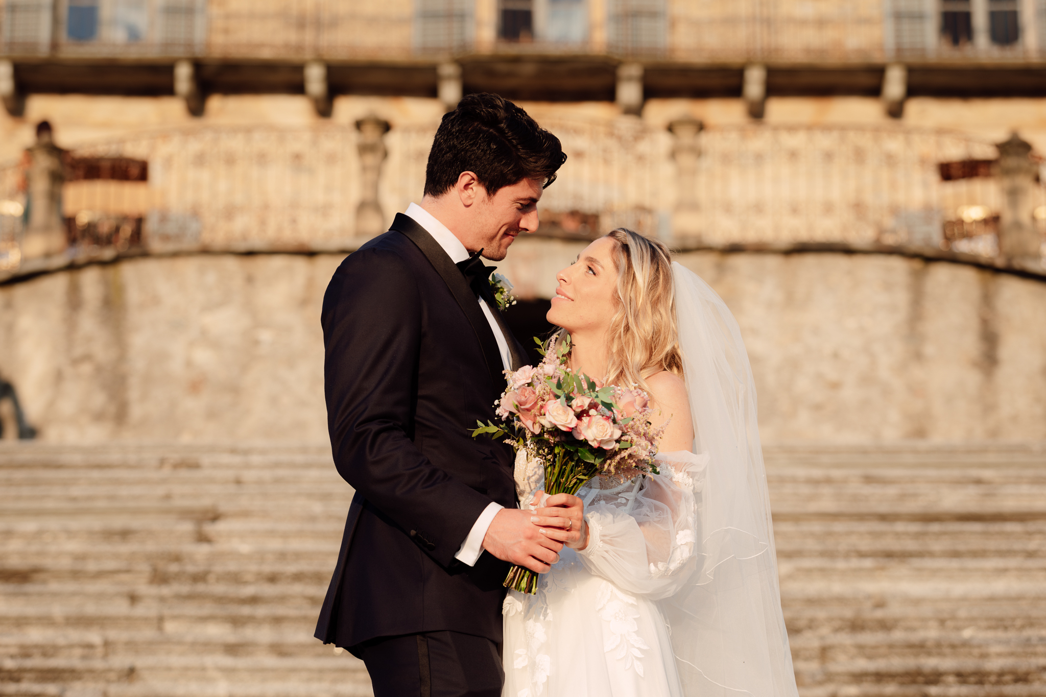 Beatrice e Conrad si guardano negli occhi alla luce dorata del tramonto, davanti alla villa.