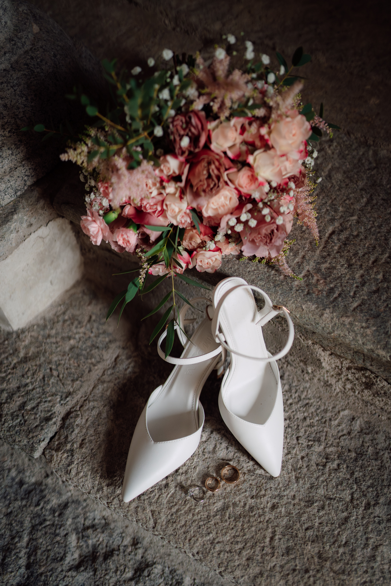 Scarpe bianche da sposa accanto al bouquet e alle fedi, simbolo di eleganza e amore nei preparativi di nozze.
