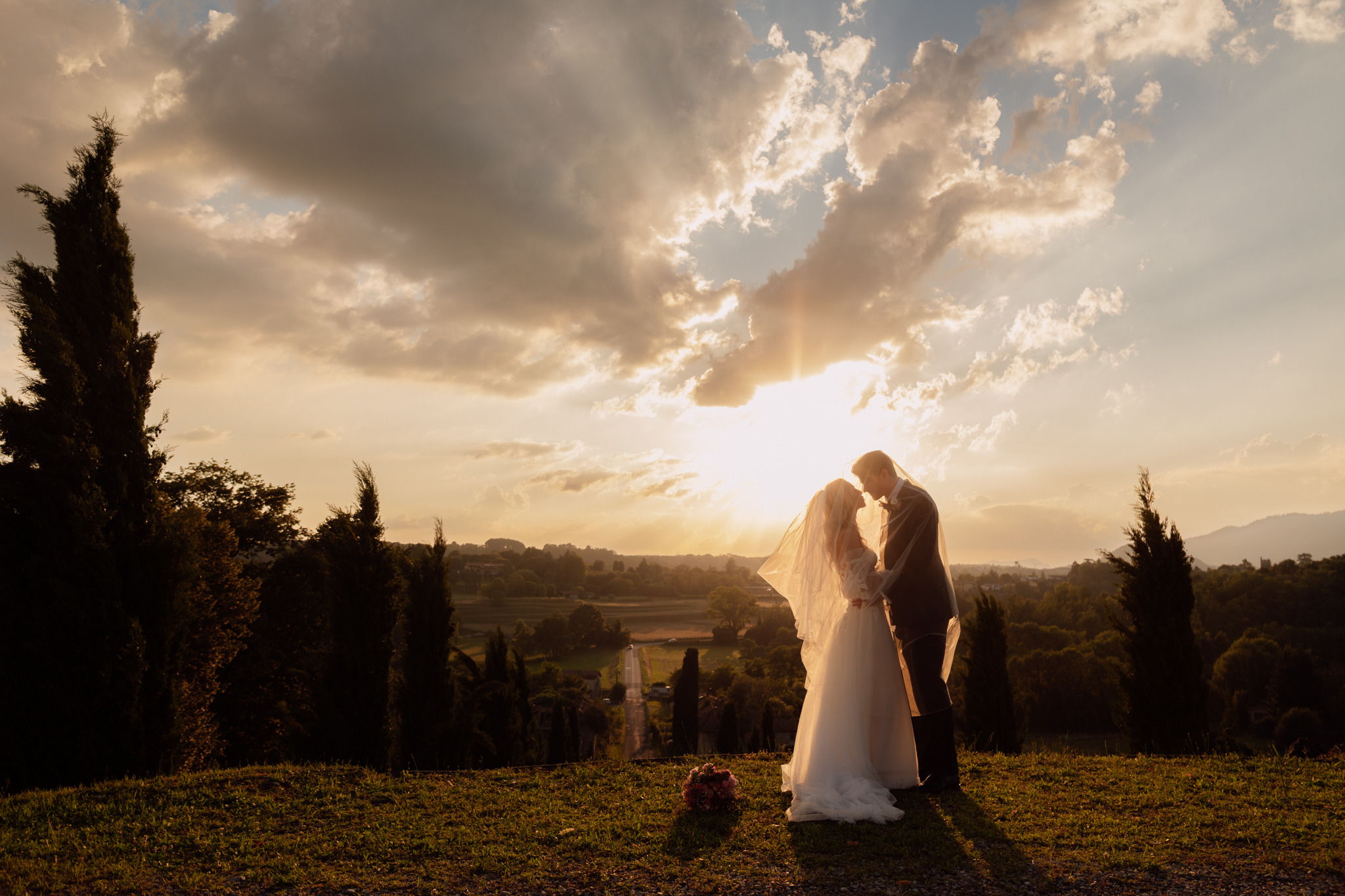Sposi al tramonto tra i cipressi, abbracciati sotto un cielo dorato.