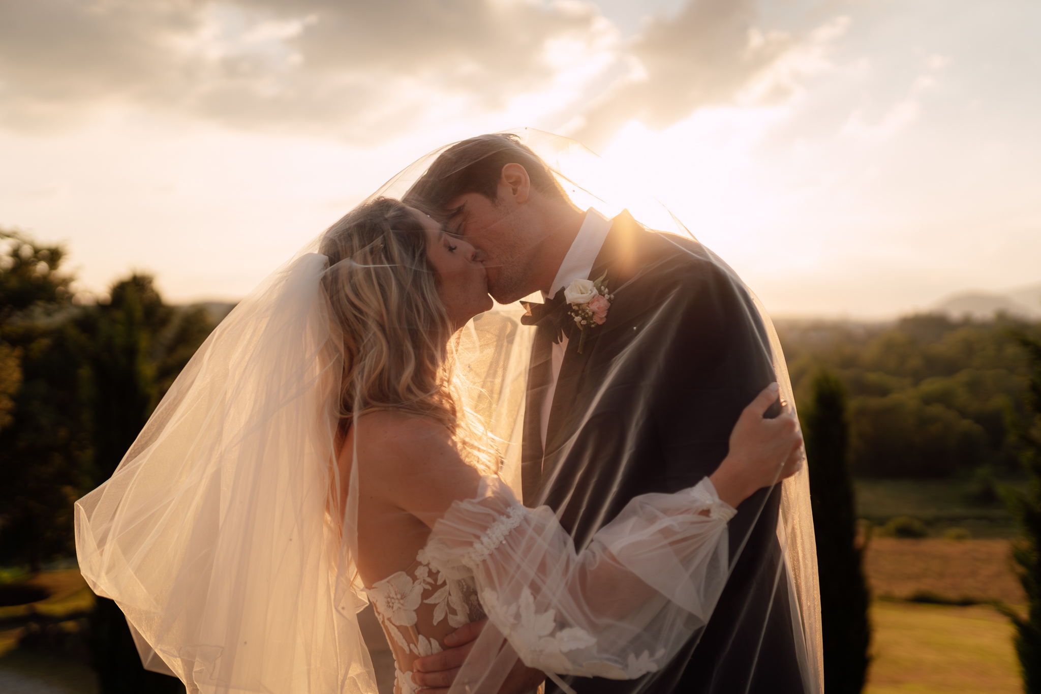 Primo piano degli sposi che si baciano sotto il velo al tramonto.