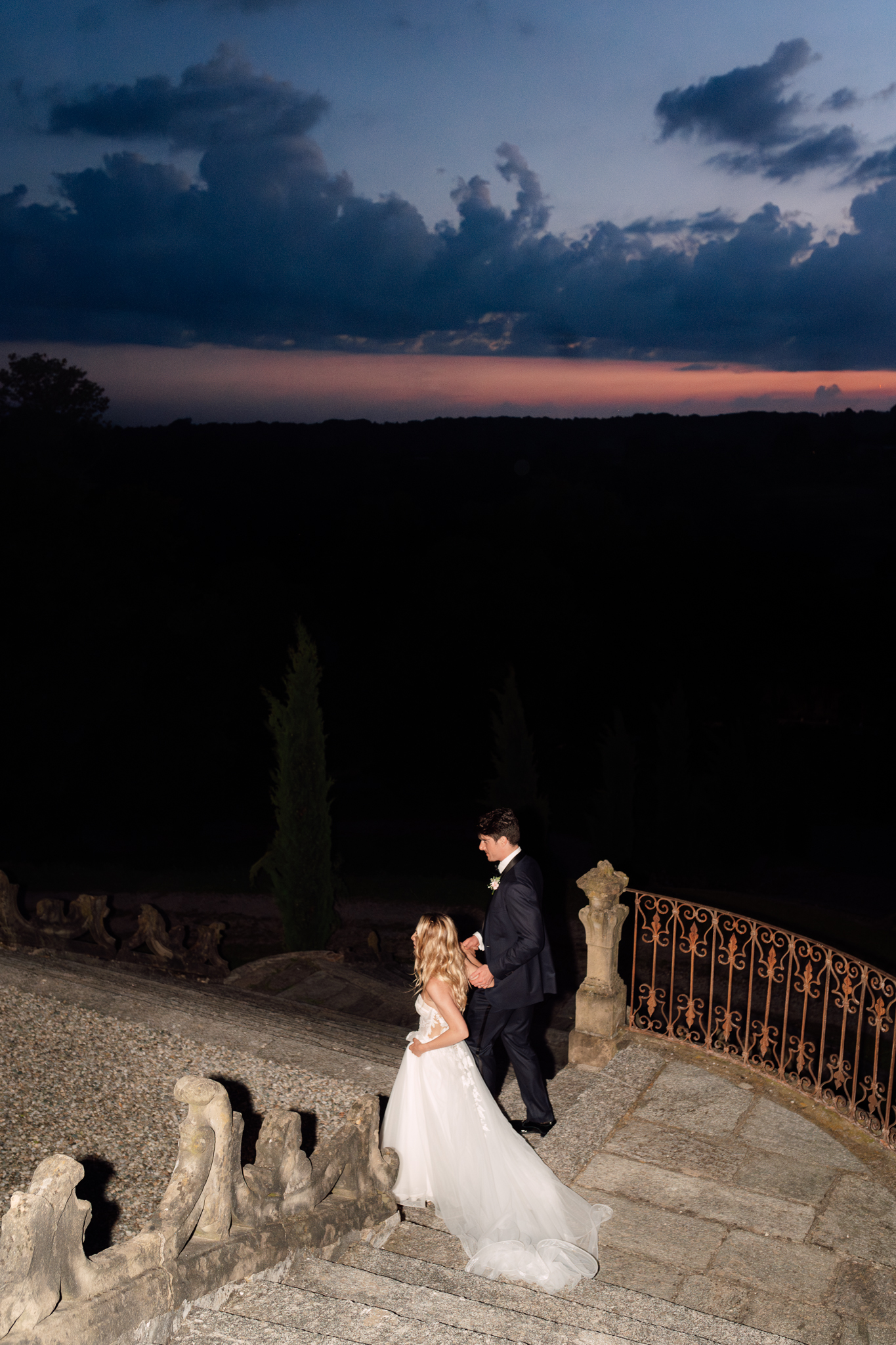 Sposi si tengono per mano al crepuscolo con cielo blu e rosa.