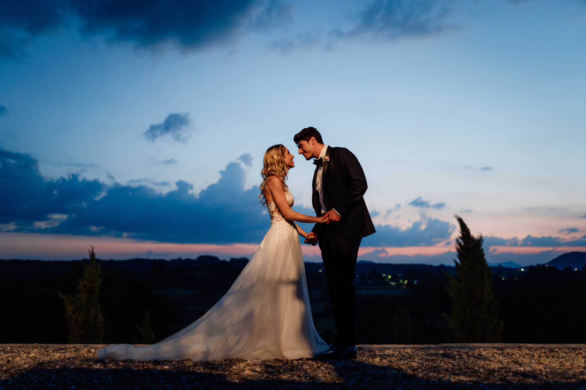 Sposi si tengono per mano al crepuscolo con cielo blu e rosa.