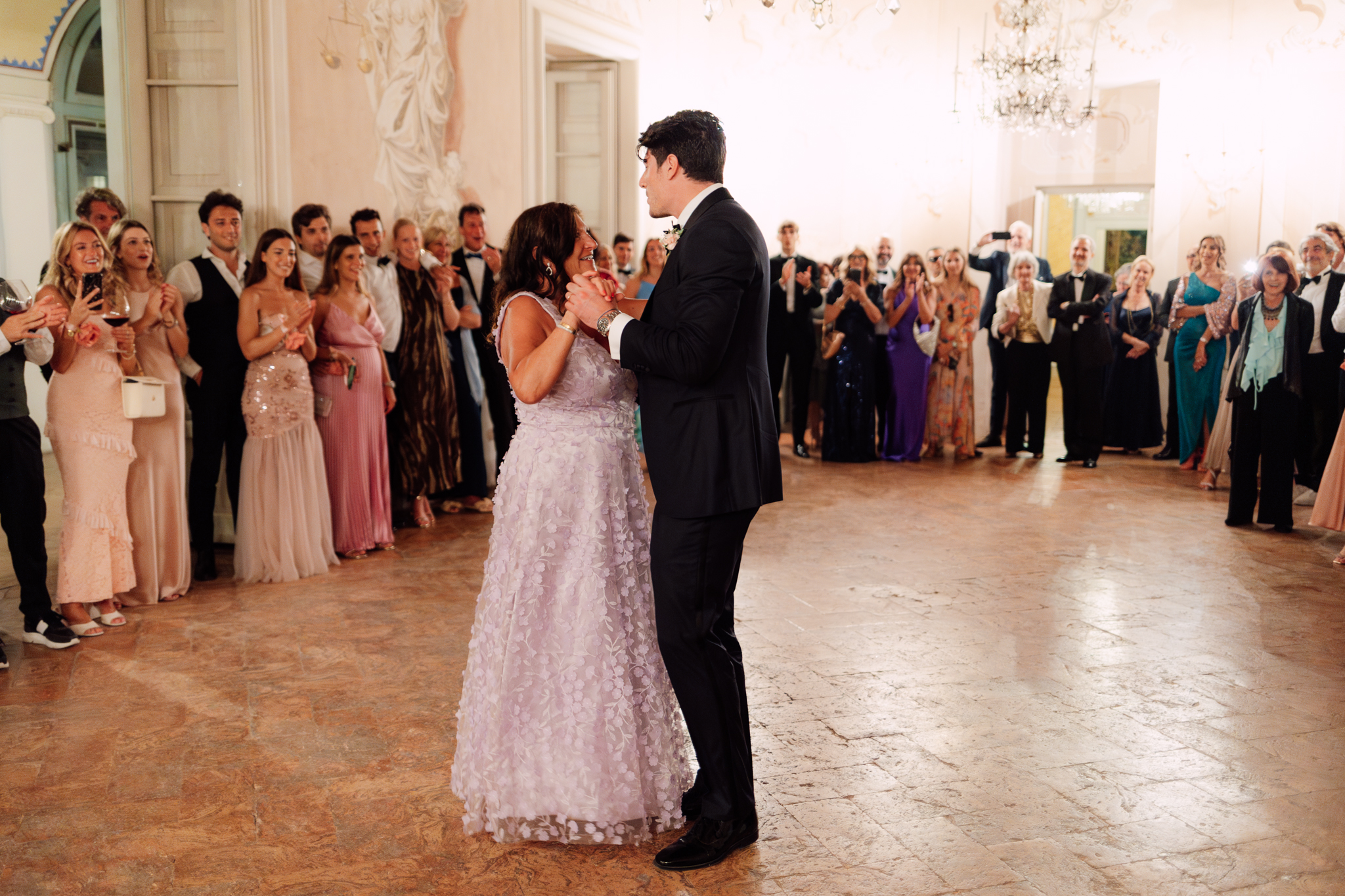 Lo sposo balla con la madre tra gli applausi degli invitati nella sala illuminata.