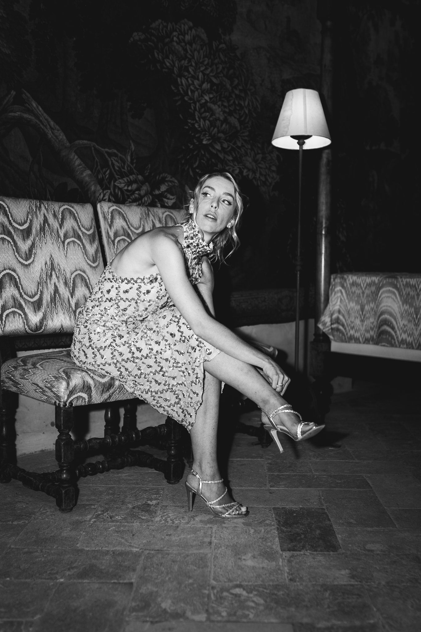 Ritratto in bianco e nero della sposa seduta mentre si sistema le scarpe.