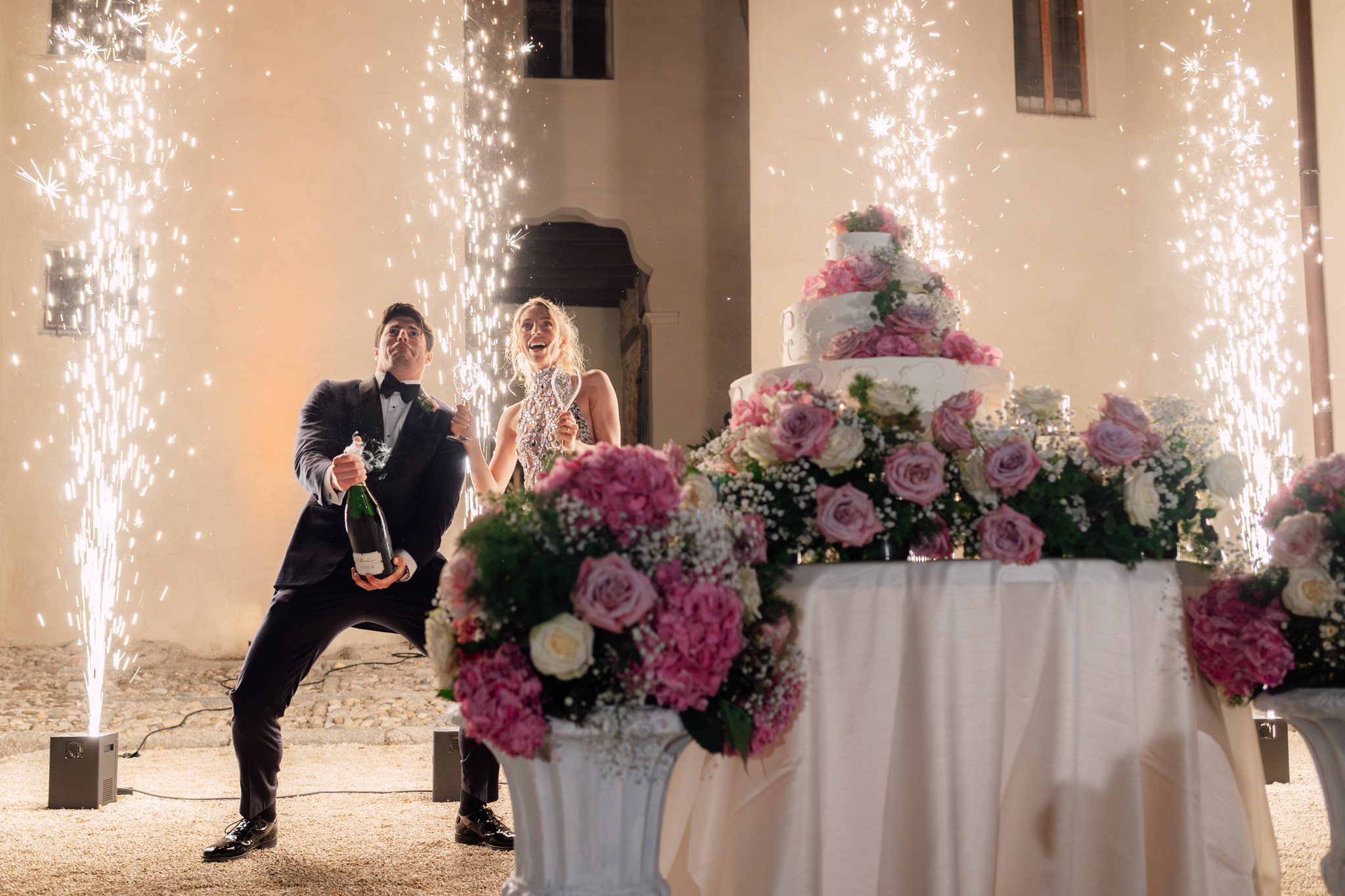 Gli sposi festeggiano con lo champagne accanto alla torta nuziale e agli effetti luminosi.