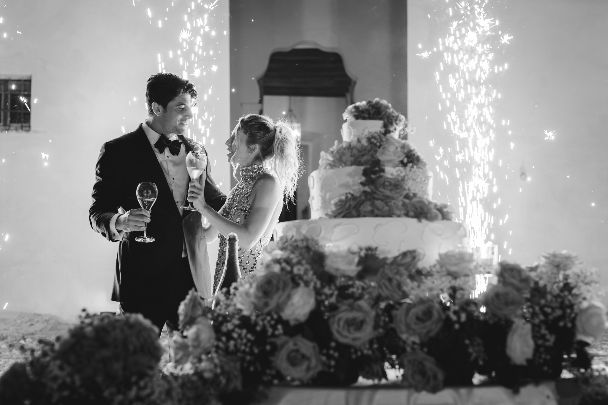 Beatrice e Conrad brindano accanto alla torta nuziale illuminata da scintille durante la festa serale.