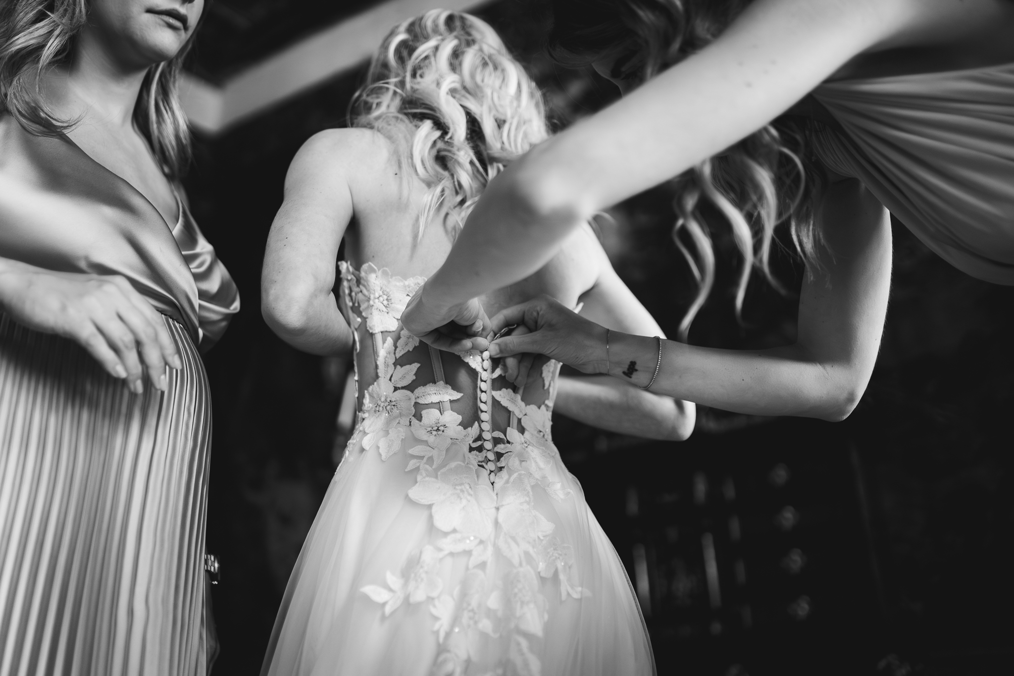 Le amiche aiutano la sposa a chiudere l’abito prima della cerimonia, momento intimo e carico di emozione.