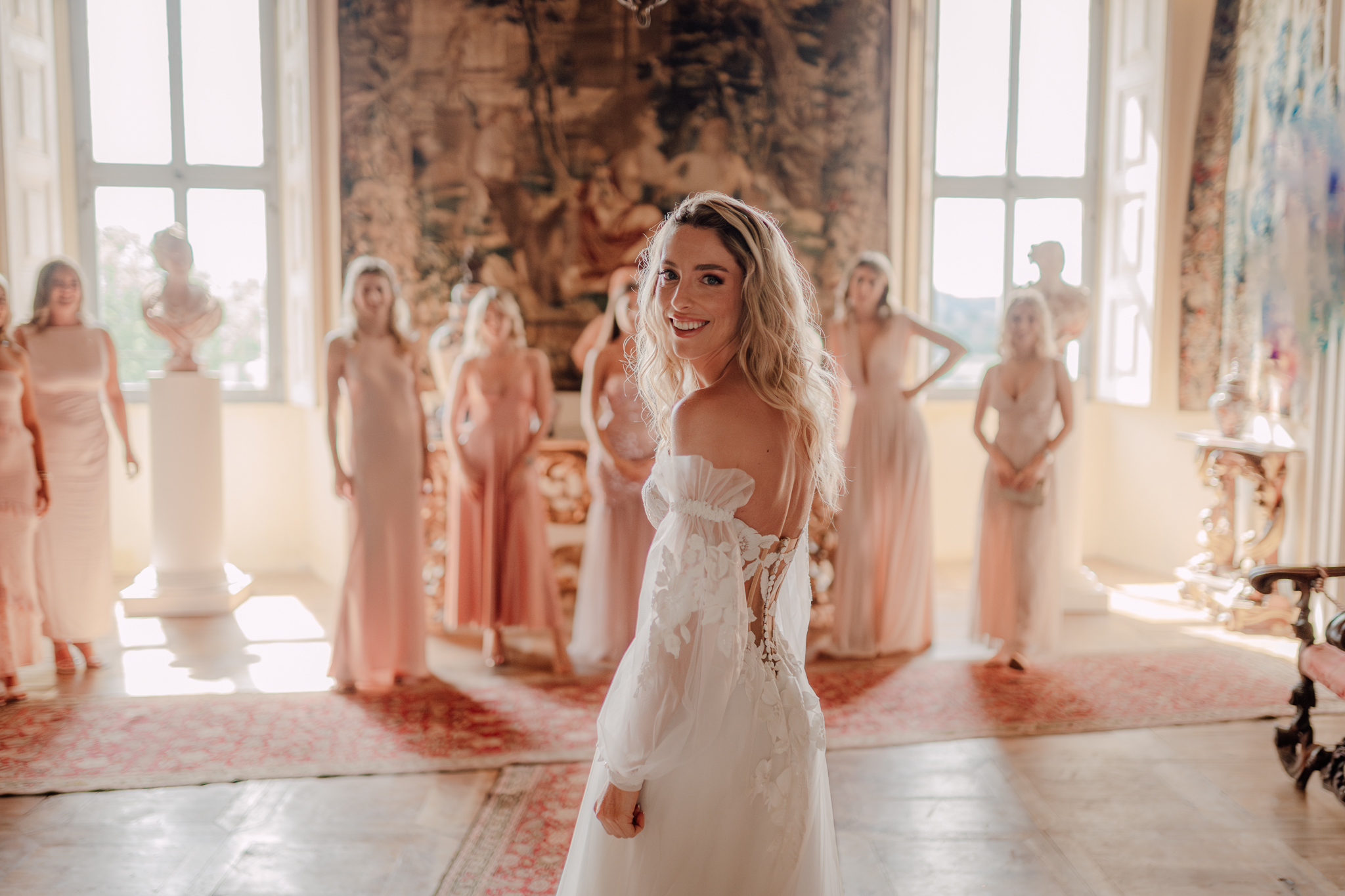 La sposa sorride circondata dalle damigelle in abiti rosa, scena luminosa e piena di emozione.